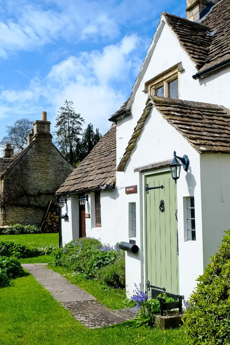 Charming countryside cottages with green doors, stone walls and landscaped gardens on a sunny day.