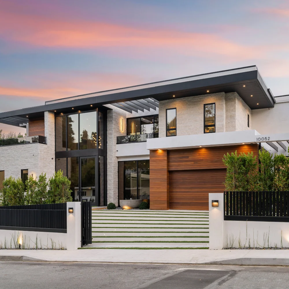 Luxury modern home with gated entrance and illuminated exterior at sunset