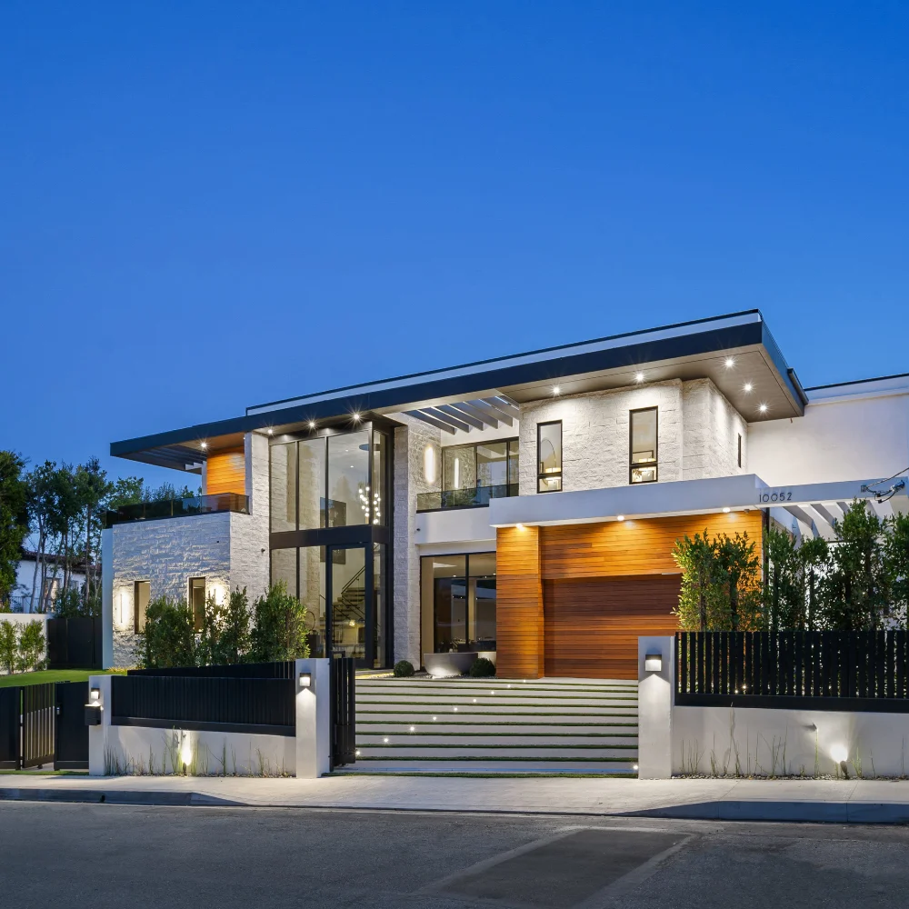 Contemporary illuminated home exterior with gated driveway and evening sky