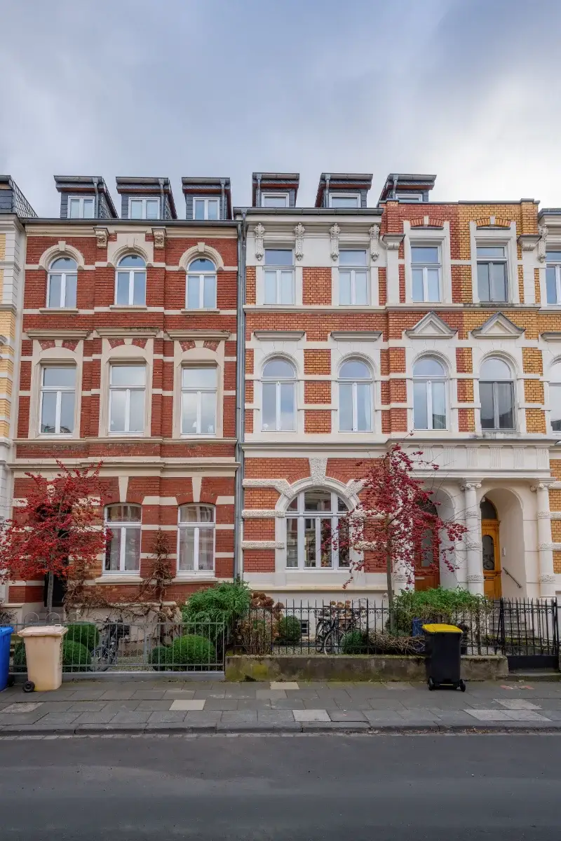 Colourful period houses with red and yellow brick façades, arched windows, decorative stonework and small front gardens.