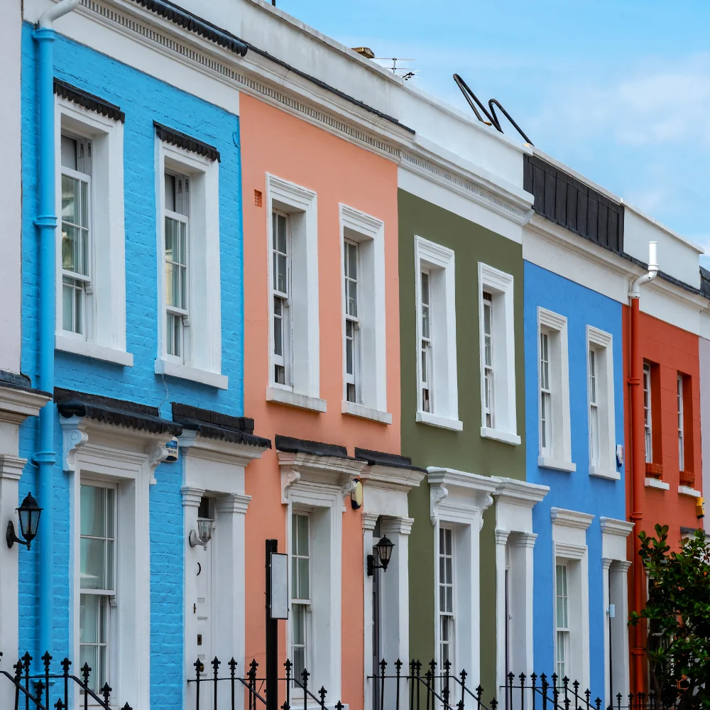 Colourful terraced houses with white-framed windows and black railings on a residential street in Notting Hill.