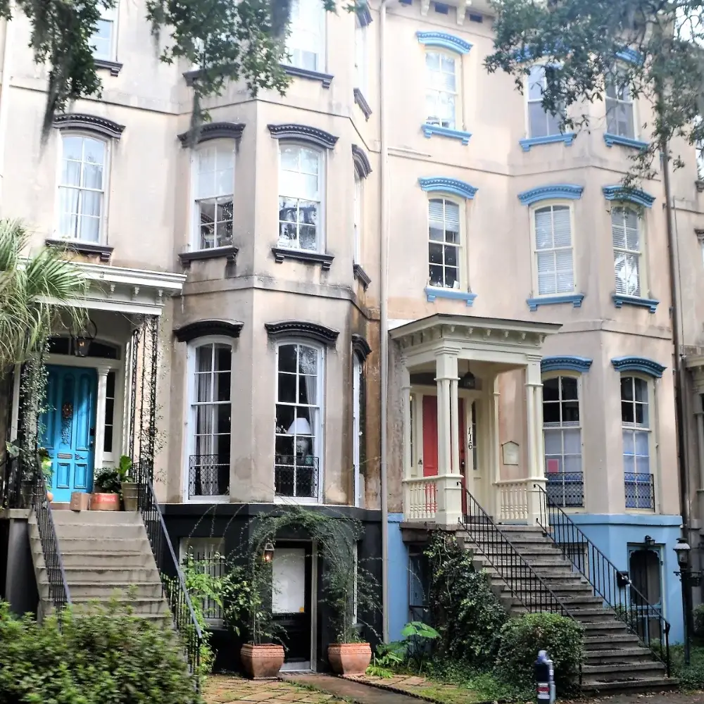 Historic townhouses with raised front entrances, tall sash windows, blue door and landscaped greenery.