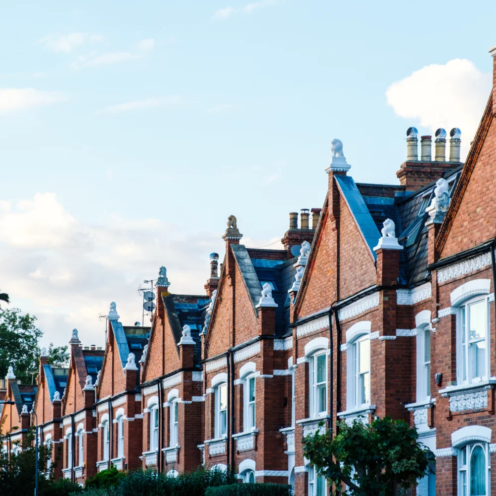 Row of red brick terraced houses with steep gable roofs, white window frames and decorative roof details.