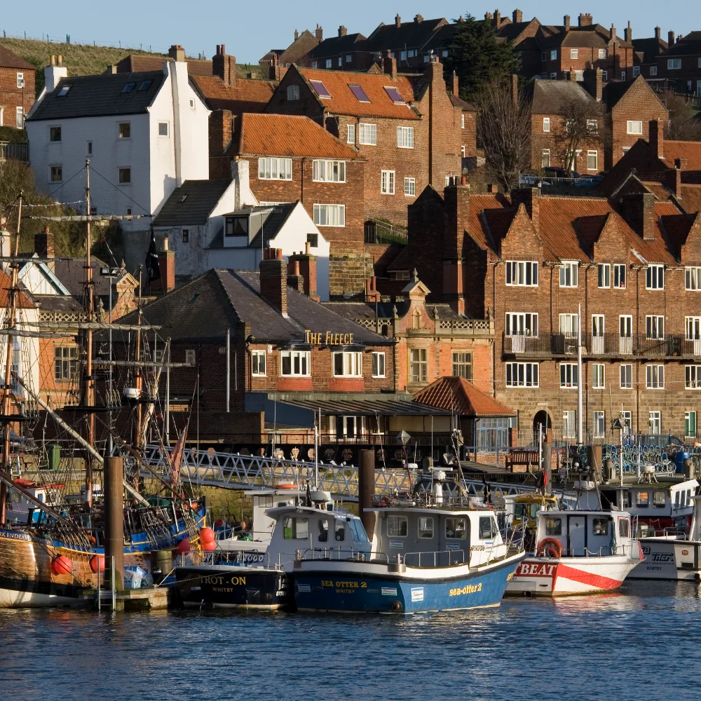 Whitby harbour with fishing boats, red brick hillside houses and waterfront buildings in North Yorkshire.